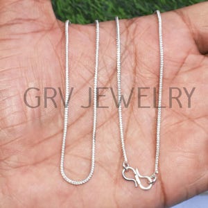 Puede incluir: Dos cadenas de plata con un cierre de langosta en un extremo. Las cadenas est&aacute;n sobre la mano de una persona.