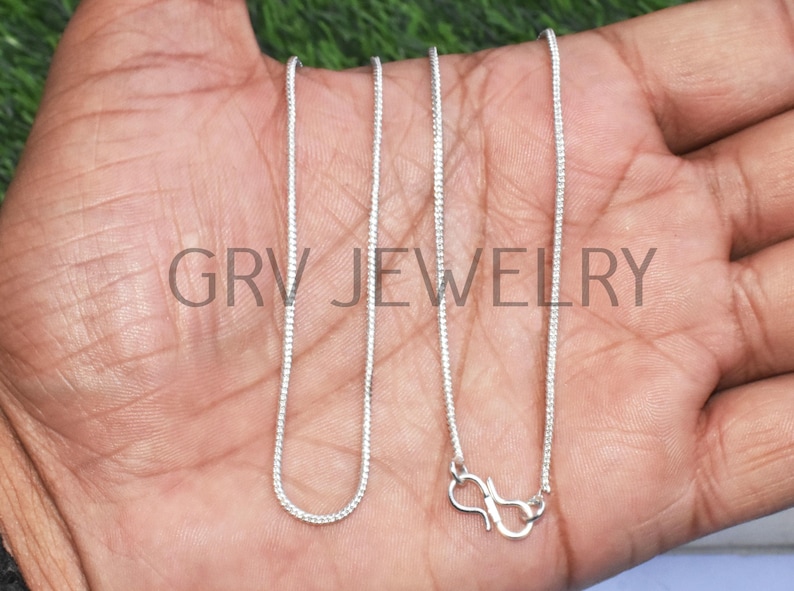 Puede incluir: Dos cadenas de plata con un cierre de langosta en un extremo. Las cadenas est&aacute;n sobre la mano de una persona.