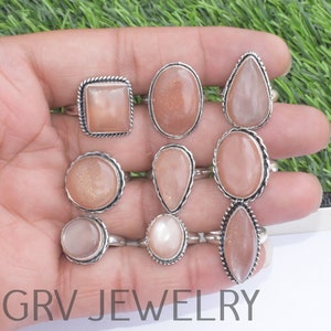 May include: A collection of nine rings with various shapes of peach-colored gemstones set in silver-toned metal. The gemstones include oval, teardrop, and square shapes. The rings are displayed on a hand against a green and white background. The text "GRV JEWELRY" is visible.