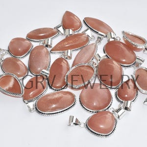 Puede incluir: Una colecci&oacute;n de 17 colgantes de piedra de sol con engastes de plata. Los colgantes son de diversas formas y tama&ntilde;os, con una mezcla de tonos naranja, rojo y marr&oacute;n.