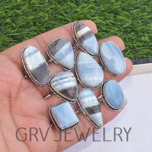 May include: A collection of nine silver rings with blue and white opal gemstones. The rings are displayed on a hand, with the gemstones facing the camera. The rings are all different shapes and sizes, but they all have a similar style.