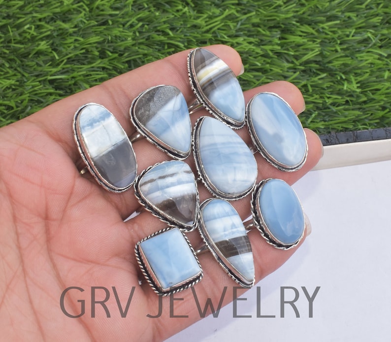 May include: A collection of nine silver rings with blue and white opal gemstones. The rings are displayed on a hand, with the gemstones facing the camera. The rings are all different shapes and sizes, but they all have a similar style.
