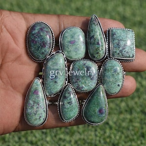 Può includere: Una collezione di anelli con pietre preziose con montature color argento. Gli anelli presentano pietre ovali, quadrate e a forma di goccia in tonalità verdi con inclusioni rosse. Gli anelli sono esposti su una mano.