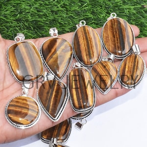 Può includere: Una collezione di ciondoli in occhio di tigre con montature in argento. I ciondoli sono di varie forme e dimensioni, tra cui ovale, a goccia e rotondo.