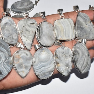 May include: A collection of silver-toned pendants with gray and white druzy stone centers. The pendants vary in shape, including oval, teardrop, and rectangular designs. Each pendant has a silver border and a loop for a chain.