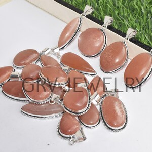 Puede incluir: Una colecci&oacute;n de 12 colgantes de piedra de sol de forma ovalada con engastes de plata. Los colgantes son de color melocot&oacute;n claro con un acabado brillante.
