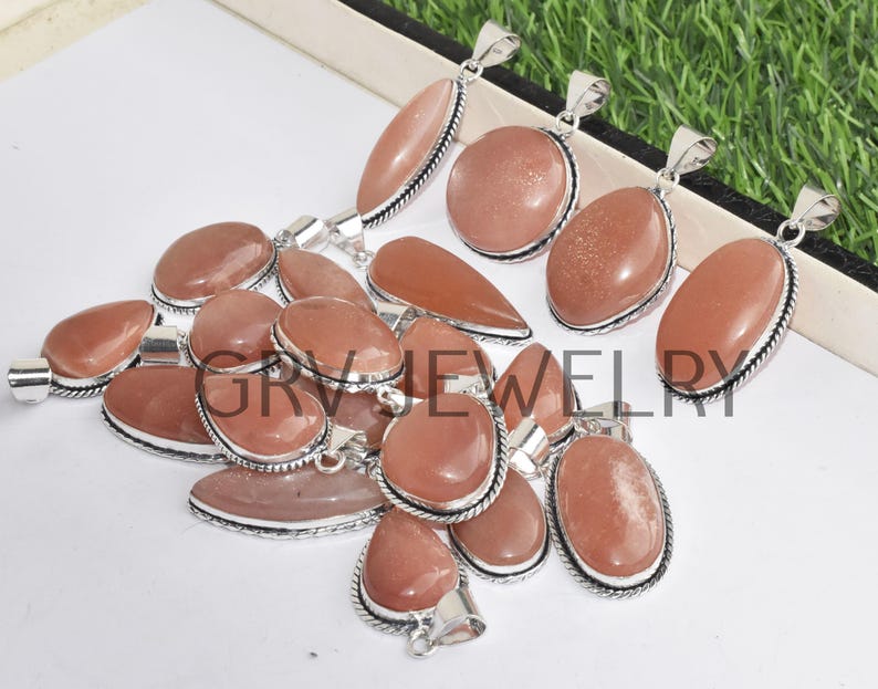 Puede incluir: Una colecci&oacute;n de 12 colgantes de piedra de sol de forma ovalada con engastes de plata. Los colgantes son de color melocot&oacute;n claro con un acabado brillante.