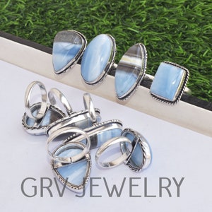 May include: A collection of silver rings with blue opal gemstones. The rings are displayed on a white surface with the text "GRVJWELRY" printed on the bottom.