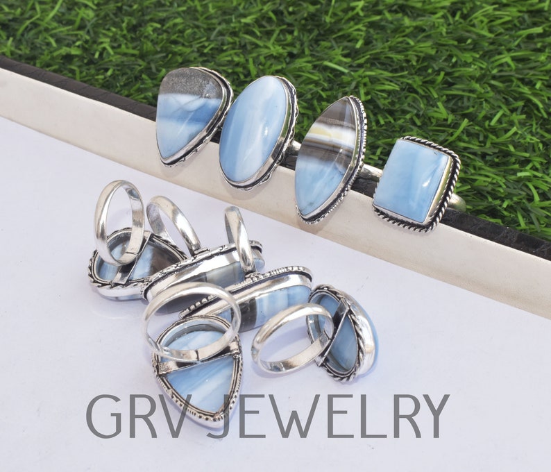 May include: A collection of silver rings with blue opal gemstones. The rings are displayed on a white surface with the text "GRVJWELRY" printed on the bottom.