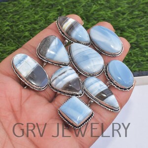 May include: A collection of ten silver rings with blue and white opal gemstones. The rings are displayed on a hand.