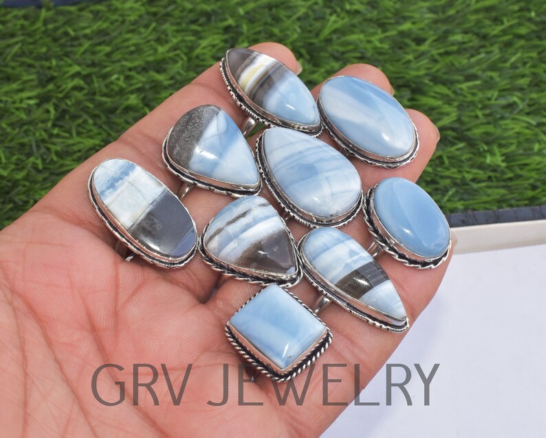May include: A collection of ten silver rings with blue and white opal gemstones. The rings are displayed on a hand.