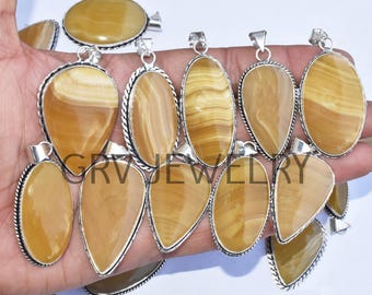 Può includere: Una collezione di nove ciondoli in agata gialla con montature in argento. I ciondoli sono di forme e dimensioni diverse e sono disposti in fila su una mano.