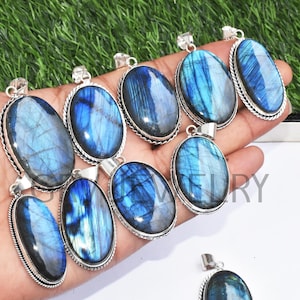 Può includere: Una collezione di nove ciondoli ovali in labradorite con montature in argento. I ciondoli sono esposti su una mano, con le pietre che mostrano una varietà di colori iridescenti blu e verdi.