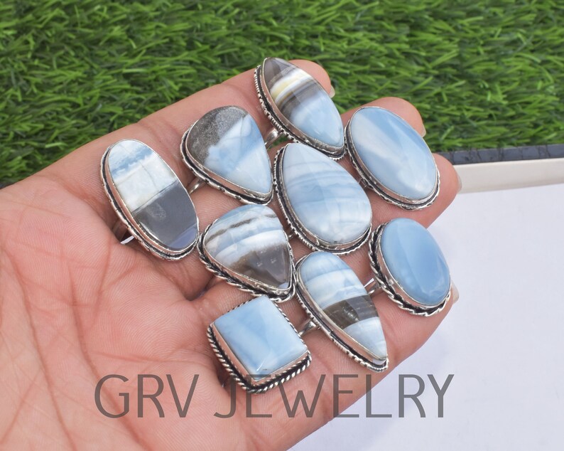 May include: A collection of ten silver rings with blue opal gemstones. The rings feature various shapes and sizes of opal stones, including oval, teardrop, and square.