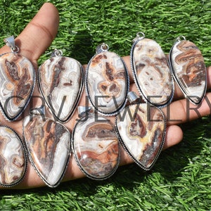 Puede incluir: Una colección de nueve colgantes de plata con piedras de ágata marrón y blanca con intrincados patrones. Los colgantes son de forma de lágrima y ovalados.