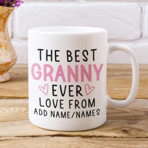 Peut inclure: Un mug en céramique blanche avec une anse, portant l'inscription THE BEST en noir, GRANNY en rose, EVER en noir, deux petits cœurs roses, et le texte LOVE FROM ADD NAME/NAMES en noir imprimé sur la face avant de l'objet.