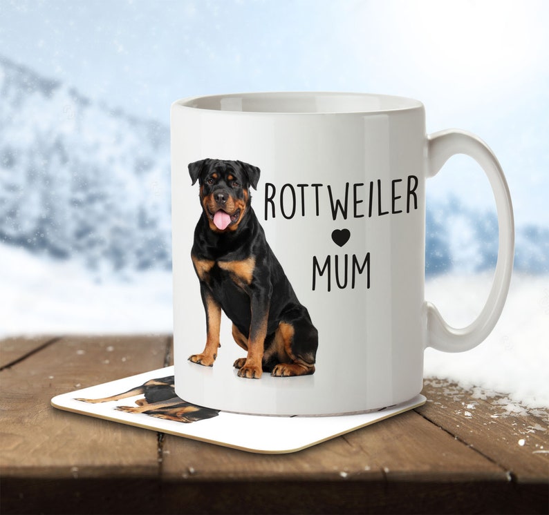 Op de afbeelding: Witte keramische mok met een afbeelding van een zwarte Rottweiler-hond en de tekst "Rottweiler Mum" met een zwart hart.