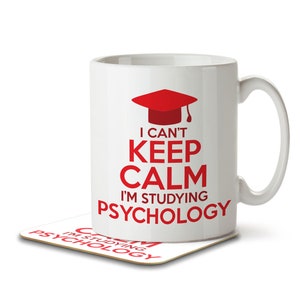 Peut inclure: Une tasse en céramique blanche avec un bonnet de graduation rouge et le texte "Je ne peux pas rester calme, j'étudie la psychologie". La tasse est posée sur un dessous-de-verre avec le même texte.