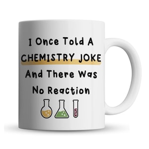 May include: White ceramic mug with a black and gold design. The mug reads "I Once Told A CHEMISTRY JOKE And There Was No Reaction". Three small beaker icons are below the text.