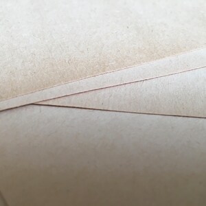 May include: Close-up of a stack of brown cardboard paper. The paper has a rough texture and is slightly worn.