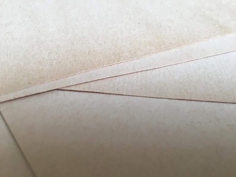 May include: Close-up of a stack of brown cardboard paper. The paper has a rough texture and is slightly worn.