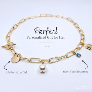 May include: Gold chain necklace with a toggle clasp, a small padlock charm, a round disc charm, a pearl charm, and a blue gemstone charm. The text "Perfect Personalized Gift for Her" and "LOVE" are visible on the image. The text "Add Initial on Disk" and "Select Your Birthstone" are also visible.