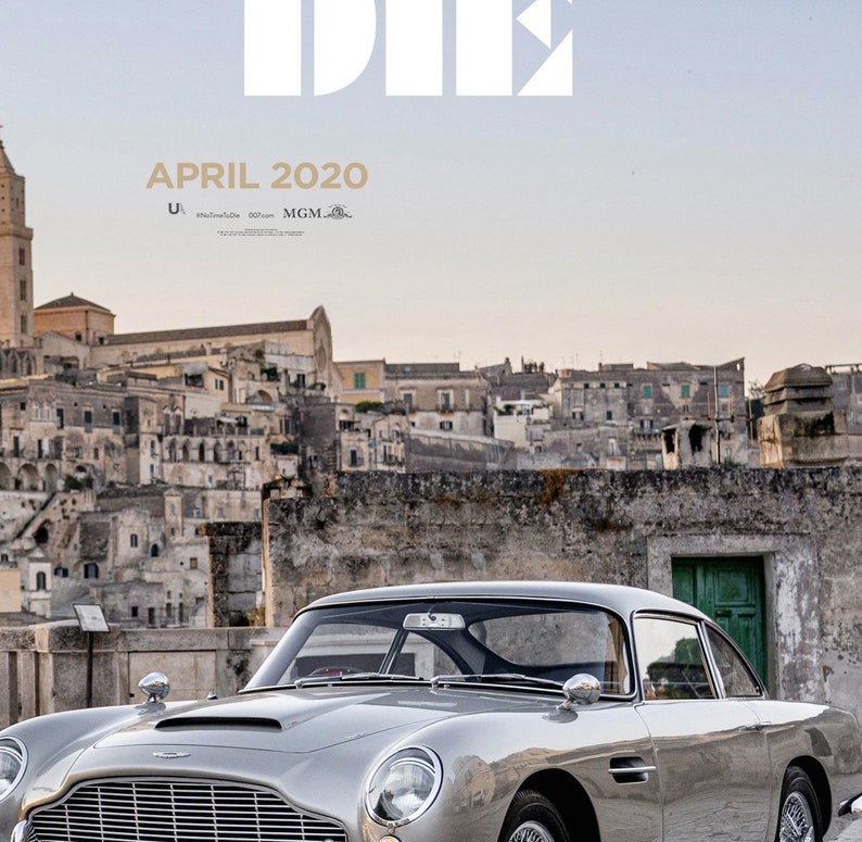 May include: A silver Aston Martin DB5 sports car parked in front of a stone building with a green door. The car has a black interior and a black roof. The building is in the background and has a cityscape behind it. The text "APRIL 2020" is at the top of the image.