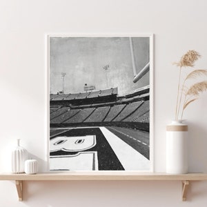 Puede incluir: Fotografía en blanco y negro de un estadio de fútbol con el campo en primer plano. El estadio está vacío y las butacas son todas negras. El campo está marcado con líneas blancas y el número "8" está pintado en el campo.