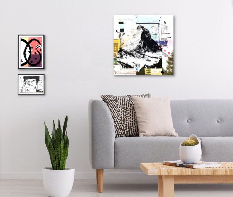 May include: Abstract art print featuring a black and white mountain illustration with colorful collage elements. Two framed prints with graphic designs are displayed on the wall. A gray sofa with decorative pillows and a wooden coffee table complete the scene.