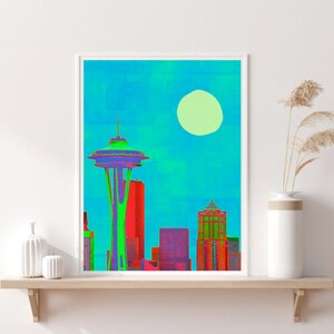 Könnte beinhalten: Ein digitaler Kunstdruck der Skyline von Seattle mit dem Space Needle im Zentrum. Der Druck zeigt einen strahlend blauen Himmel mit einer großen weißen Sonne und die Gebäude sind in Rot-, Grün- und Violetttönen gehalten.