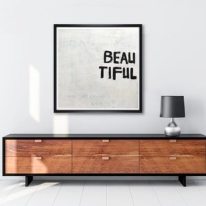 Könnte beinhalten: Ein schwarzer Rahmen um ein Leinwandbild mit weißem Hintergrund und schwarzem Text, der "Life was beautiful we just couldn't see it" lautet. Das Bild hängt an einer weißen Wand über einer schwarzen Kommode mit sechs Schubladen.