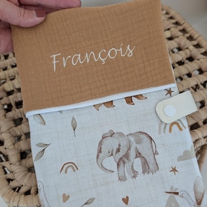 May include: A tan and white baby changing pad cover with an elephant and stork pattern. The top flap is tan with the name "Fran&ccedil;ois" embroidered in white. The cover has a white snap closure.