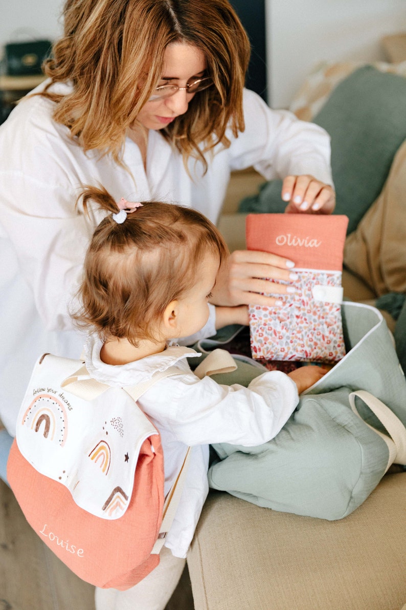 Maman, Lana qui remplissent le sac polochon avec le protège carnet de santé. Lana porte aussi un sac à dos personnalisé en double gaze de coton
