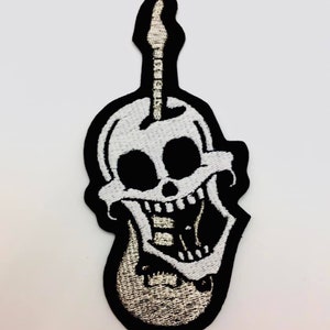 Könnte beinhalten: Ein weißer Schädel mit schwarzem Umriss und einem breiten Grinsen, der eine weiße Gitarre mit schwarzen Saiten hält. Die Gitarre ist in Form des Schädels geformt.