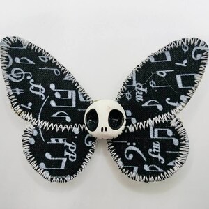 Könnte beinhalten: Schwarzer Stoffschmetterling mit weißen Noten und einem weißen Schädel mit schwarzen Augen in der Mitte.