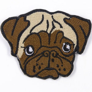 Könnte beinhalten: Gestickter Aufnäher eines braunen und beigen Mops mit schwarzen Augen. Der Aufnäher ist perfekt, um Kleidung, Taschen oder anderen Accessoires eine persönliche Note zu verleihen.