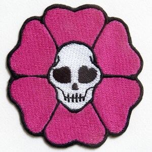 Könnte beinhalten: Eine rosa Blume mit einem weißen Totenkopf in der Mitte. Die Blume hat fünf Blütenblätter und ist schwarz umrandet.