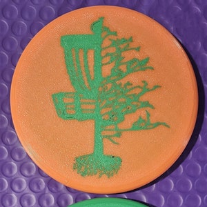 May include: Two round disc golf targets, one orange and one green, with a disc golf basket and a tree silhouette design.