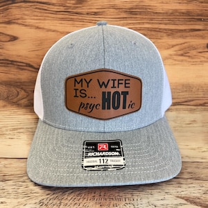 May include: A grey and white trucker hat with a brown leather patch that says "MY WIFE IS... PSYc HOT ic". The hat has a red and white label that says "EST. 1970 RICHARDSON ORIGINAL 112 TRUCKER ADJUSTABLE".