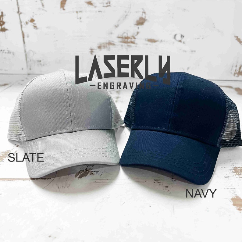 Puede incluir: Dos gorras de camionero, una gris pizarra y otra azul marino, con una parte trasera de malla. Las gorras tienen el texto "LASERLY - ENGRAVING" en la parte delantera.