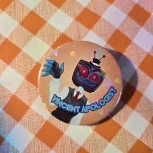 May include: A round button with a cartoon illustration of a robot-like character with a TV screen for a head. The text "Vincent Apologist" is printed on the button. The background is a peach color with a holographic effect.