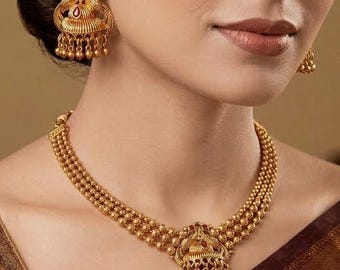 Puede incluir: Juego de joyas doradas que incluye un collar y pendientes a juego. El collar tiene un diseño de cuentas de varias hebras con un colgante. Los pendientes tienen un diseño similar con elementos colgantes. El conjunto es ornamentado y detallado.