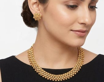 May include: A gold-colored necklace and matching earrings set. The necklace is a choker style with a beaded design. The earrings are round with a floral pattern. The jewelry is worn against a black top.