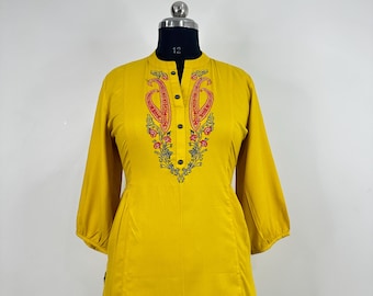 Pode incluir: Uma blusa amarela de manga comprida com um design de bordado de paisley e flores na frente. A blusa tem um fecho de botão no pescoço.