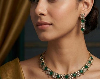 Puede incluir: Un conjunto de collar y pendientes dorados. La joyería presenta piedras cuadradas de color verde esmeralda y pequeñas piedras de acento transparentes. El collar se coloca alrededor del cuello y los pendientes cuelgan de los lóbulos. El fondo es de color dorado suave.
