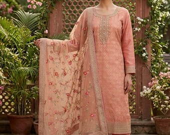 May include: A peach-colored long-sleeved tunic with a geometric pattern and intricate embroidery around the neckline, paired with matching straight-leg trousers and a sheer, floral-embroidered dupatta draped over one shoulder.