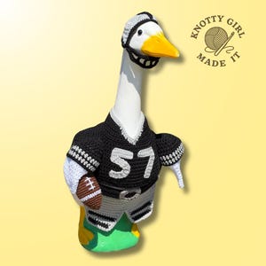 May include: A white goose figurine wearing a crocheted black and white football uniform with the number 57, a matching helmet, and holding a small brown football. The text KNOTTY GIRL MADE IT is visible in the upper right corner of the image.