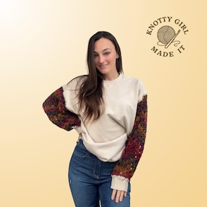 May include: Cream-colored sweatshirt with crochet sleeves in shades of burgundy, brown, and green. The sleeves are the focal point, adding a unique texture and color contrast to the casual top. The logo "KNOTTY GIRL MADE IT" is in the upper right corner.