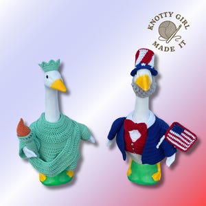May include: Two goose figurines, one dressed as the Statue of Liberty in a green crochet outfit and holding a torch, the other as Uncle Sam in a red, white, and blue outfit, holding an American flag. The logo "Knotty Girl Made It" is in the top right.