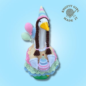 Puede incluir: Una caprichosa figura de ganso con un gorro de fiesta, trenzas y un vestido de ganchillo, sosteniendo una magdalena y globos. El ganso tiene un pico amarillo y está decorado con colores pastel. El texto "KNOTTY GIRL MADE IT" está en la esquina superior derecha.